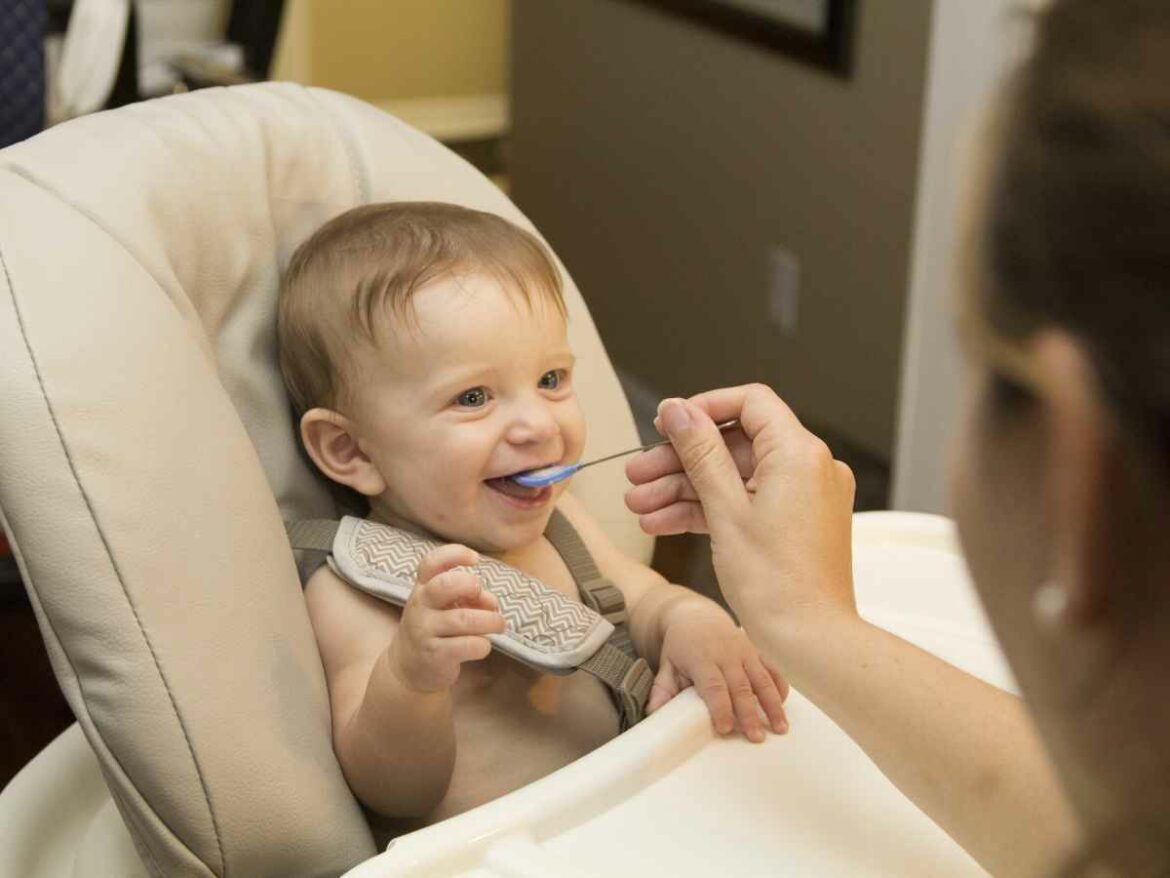 Bebê que esta passando pela introdução alimentar, sentado em seu cadeirão e sendo alimentado por sua mãe com suas receitas juninas adaptada.