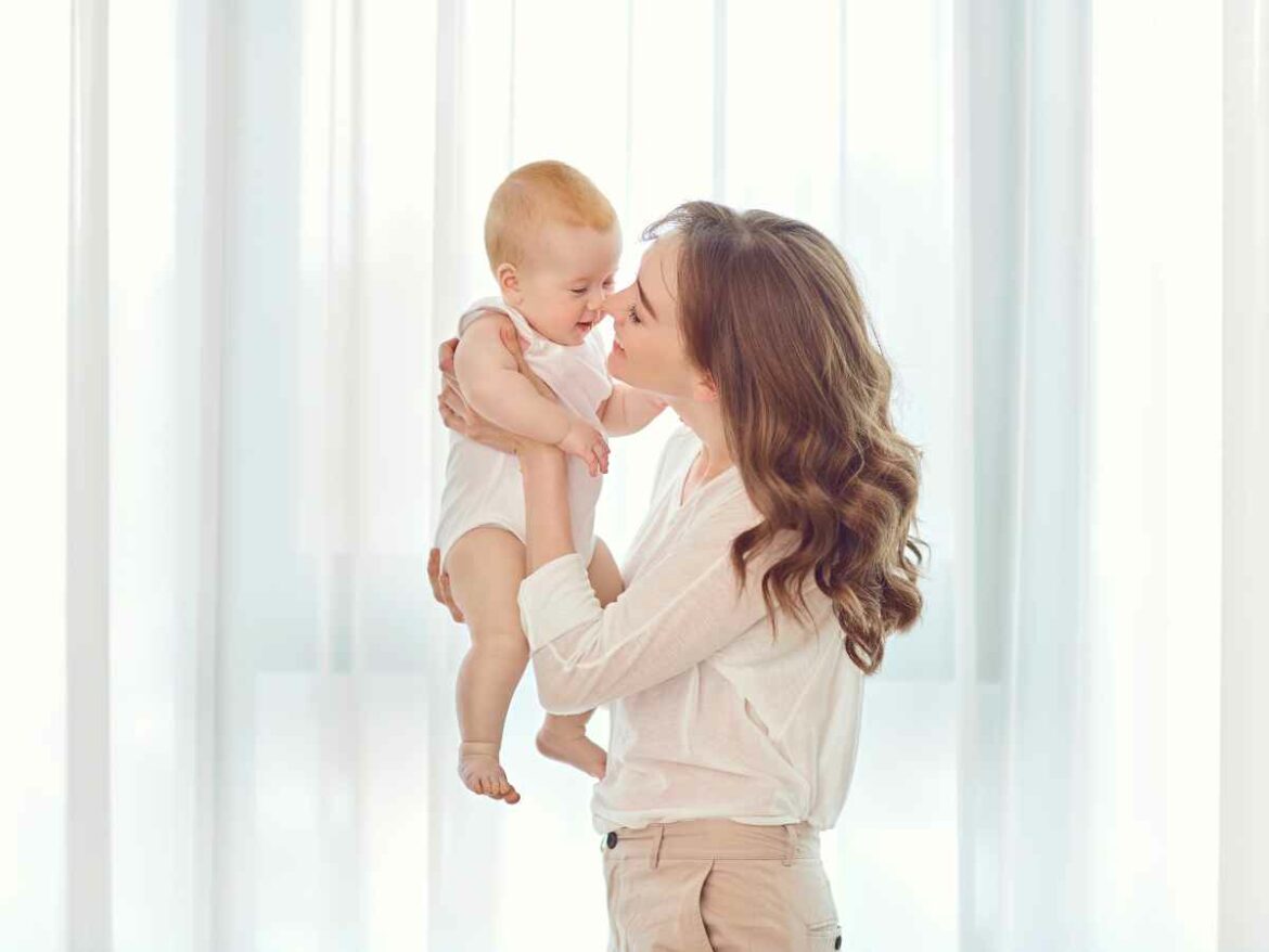 Mulher segurando seu filho no ar e beijando seu nariz, enquanto celebra o seu primeiro dia das mães.