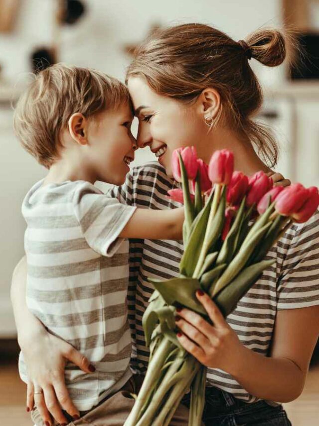 Mãe abaixad ano chão, olhando nos olhos do seu filho e segurando seu presente de dia das mães, um buque de flores.