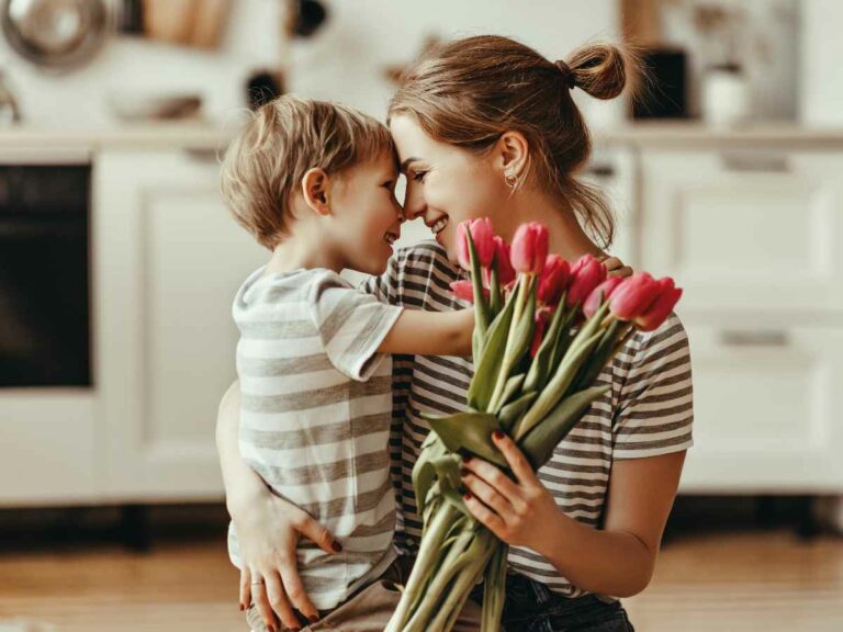 Mãe abaixad ano chão, olhando nos olhos do seu filho e segurando seu presente de dia das mães, um buque de flores.