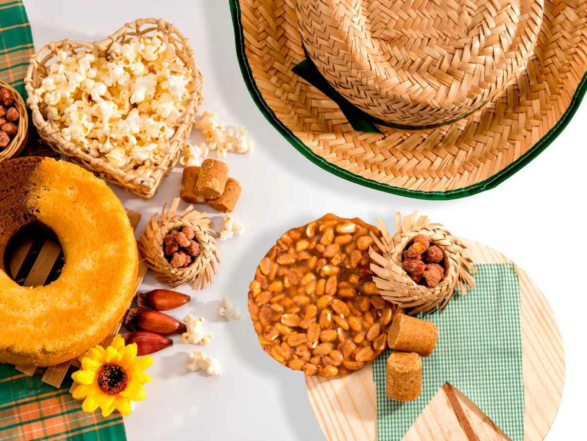 Ingredientes juninos espalhados em uma mesa: pipoca, milho, bolo de milho, pinhão e amendoim, que são usados em receitas juninas.