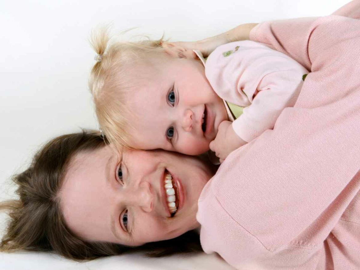 Mãe segurando filha perto do rosto, enquanto sorriem para uma foto e posam com o look combinando.