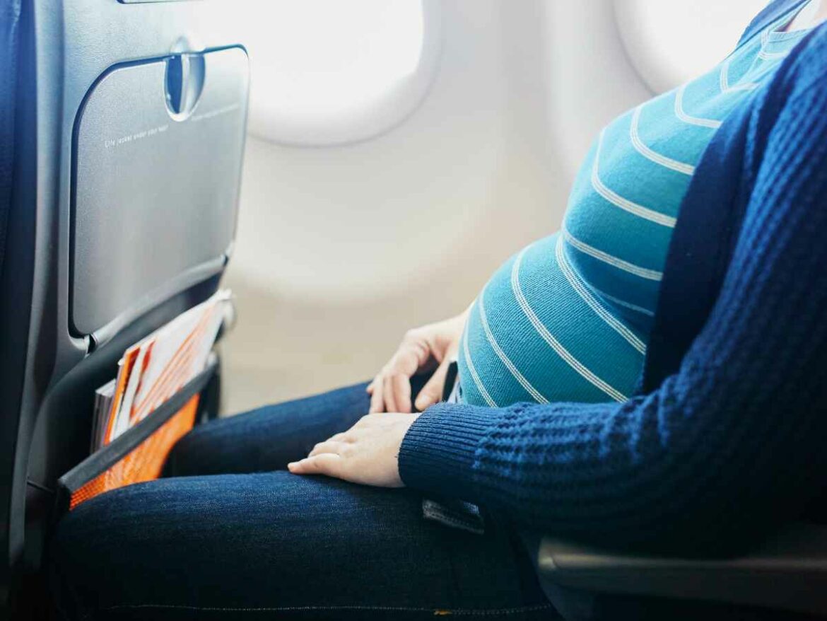 Mulher grávida sentada em assento de avião com o cinto de segurança ajustado corretamente abaixo da barriga.