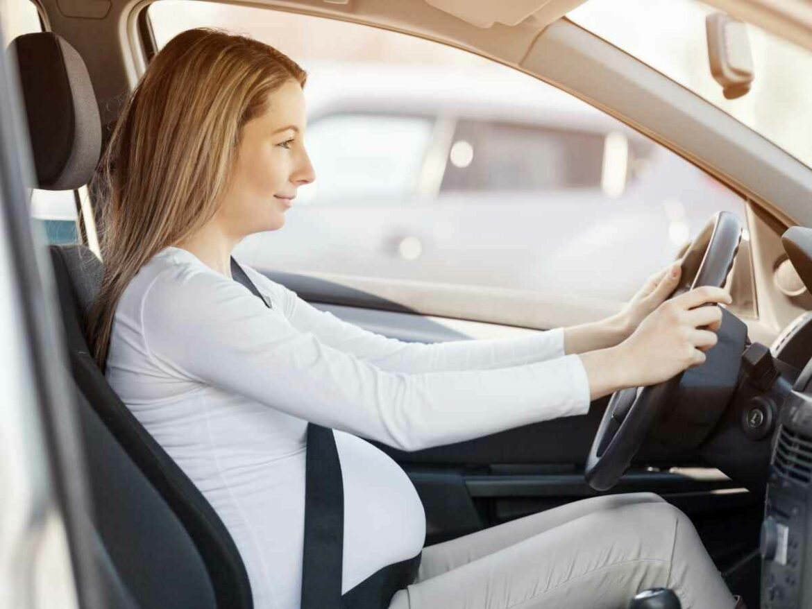 Mulher grávida dirigindo um carro com cinto de segurança corretamente posicionado abaixo da barriga.