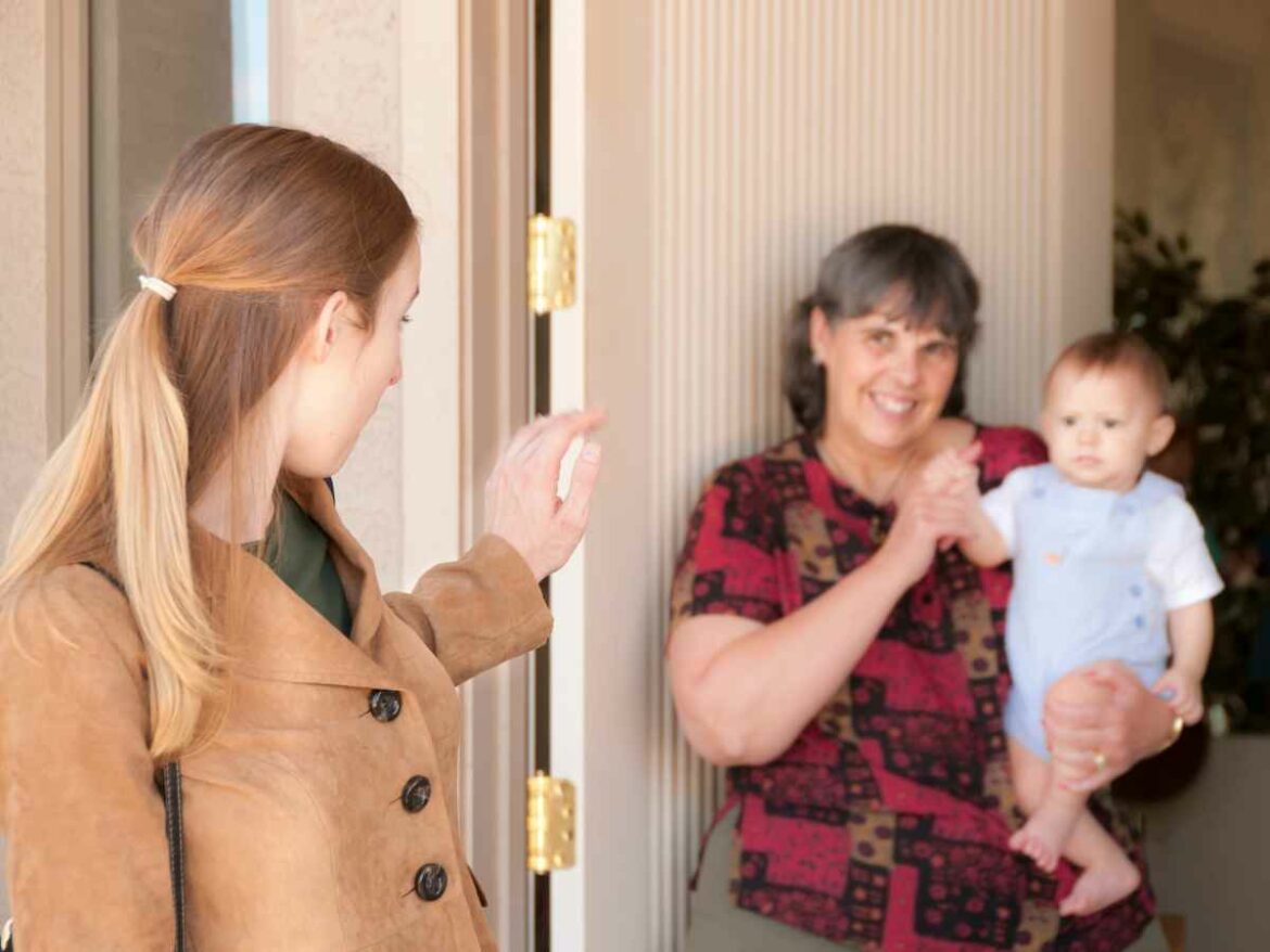 Mãe acena para o filho no colo de uma parente mais velha na porta de casa, simbolizando o retorno ao trabalho após a licença-maternidade.