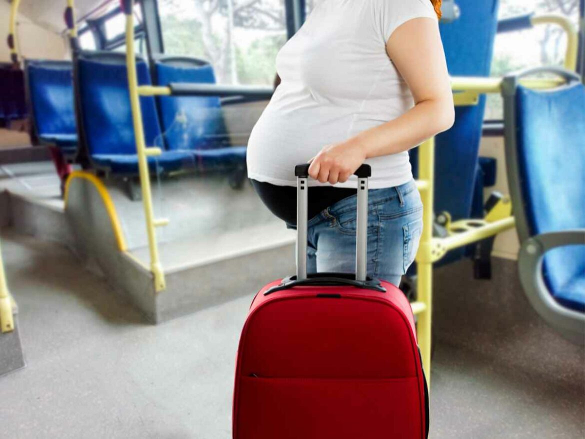 Mulher grávida segurando uma mala vermelha dentro de um ônibus.