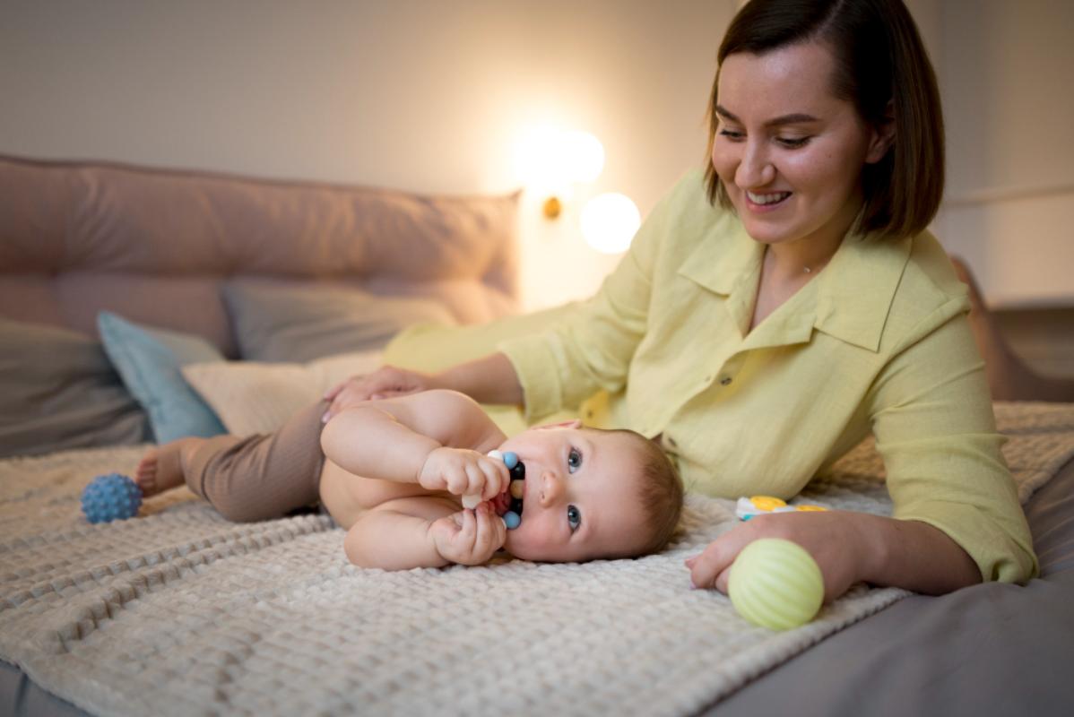 Bebê deitado na cama brincando com sua mãe.