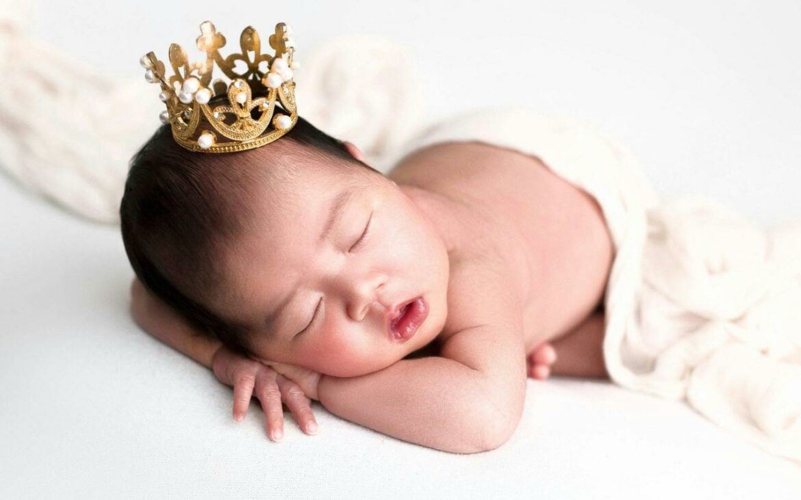 Bebê deitado e dormindo com coroa de príncipe.