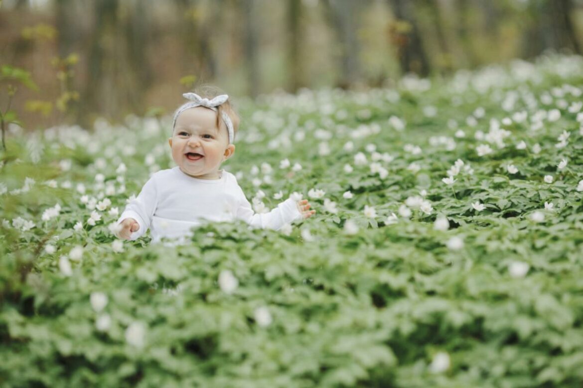 Bebê sentada no meio de um campo de flores durante a primavera.