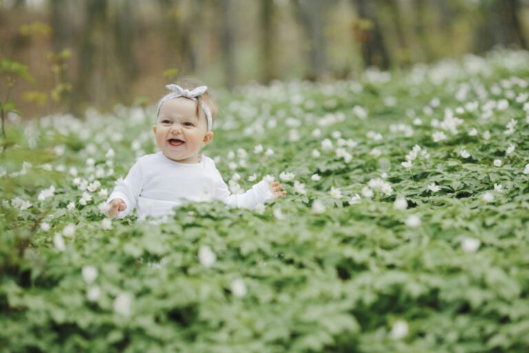 Bebê sentada no meio de um campo de flores durante a primavera.