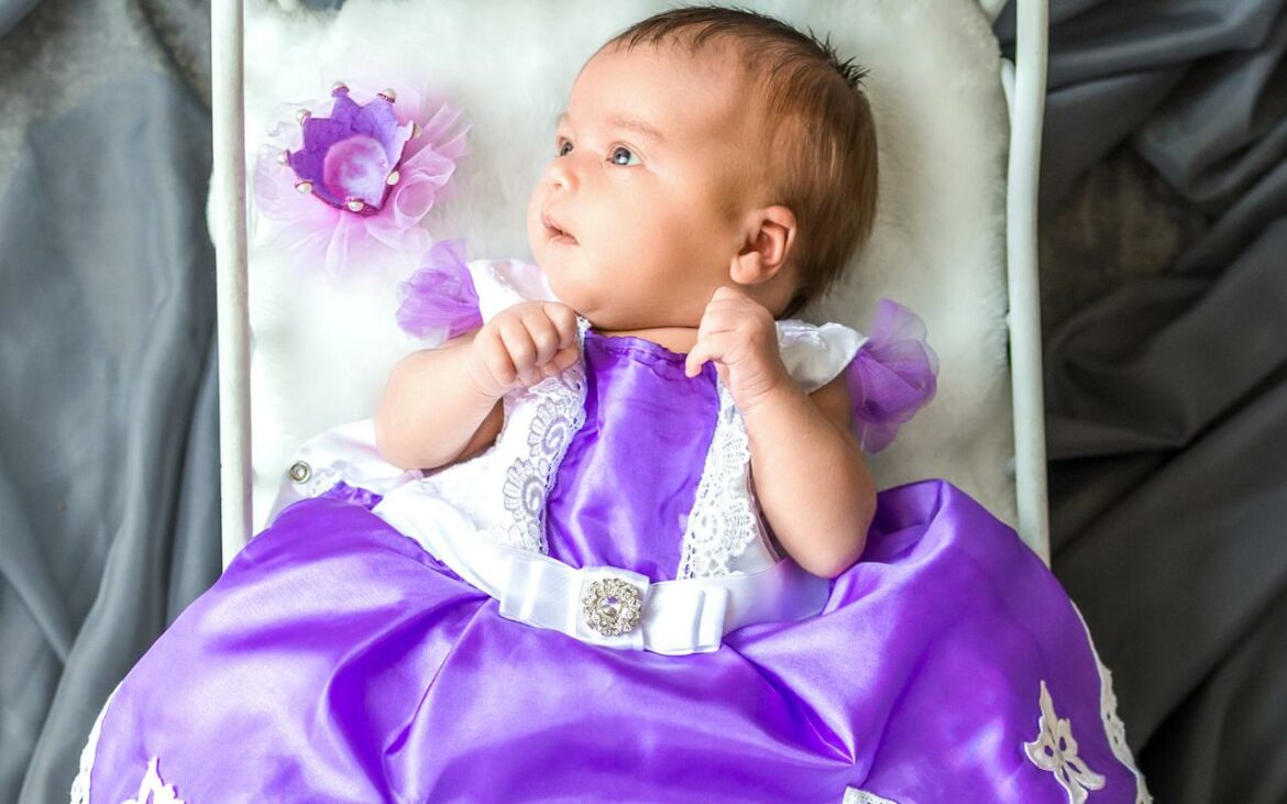 Bebê vestida de princesa, com vestido, roxo, deitada no berço.