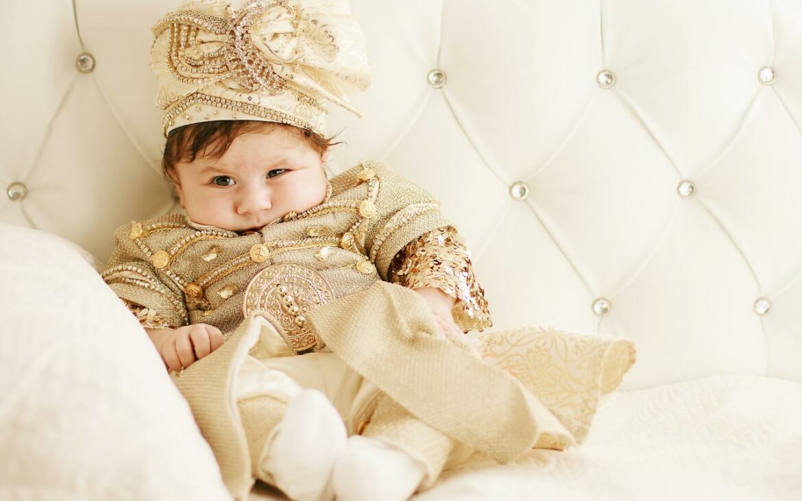 Bebê sentado na cama com roupa de príncipe.