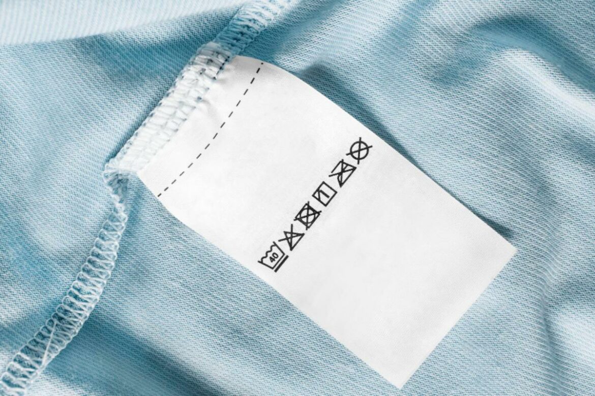 Etiqueta costurada em peça de roupa com símbolos de lavagem e cuidados têxteis, indicando instruções para conservação adequada do tecido.