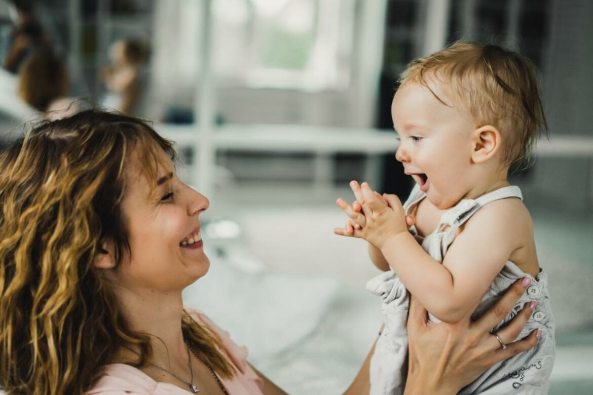 Mãe sorridente segurando bebê enquanto ele emite balbucios.