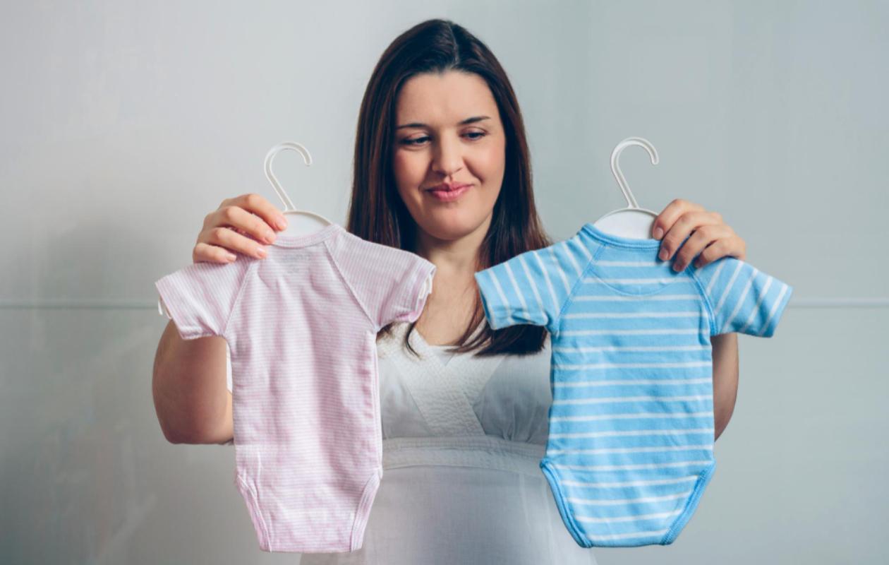 mulher segurando duas roupas de bebê, uma rosa e uma azul.