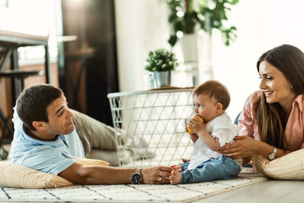 Pai e mãe deitados no chão com o bebê incentivando a fala.