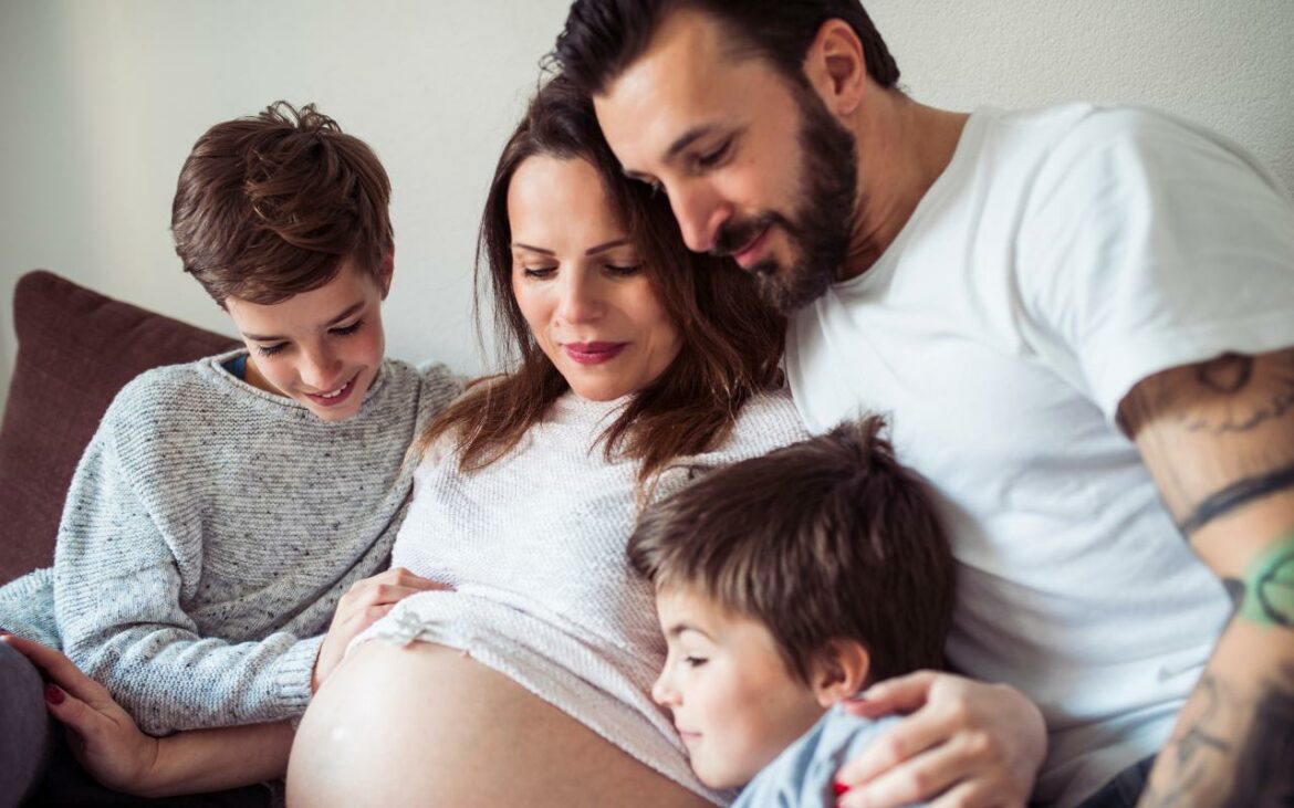 Mulher grávida na terceira gestação explicando para os filhos.