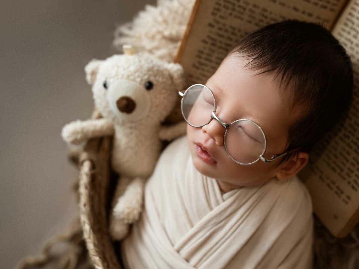 Bebê dormindo tranquilamente com óculos redondos, apoiado em uma biblia aberta.
