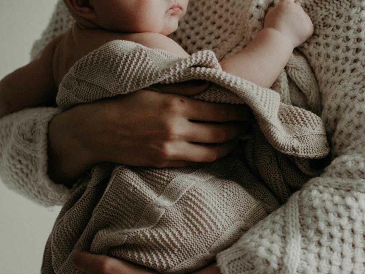 Adulto segurando um bebê envolto em manta de tricô bege