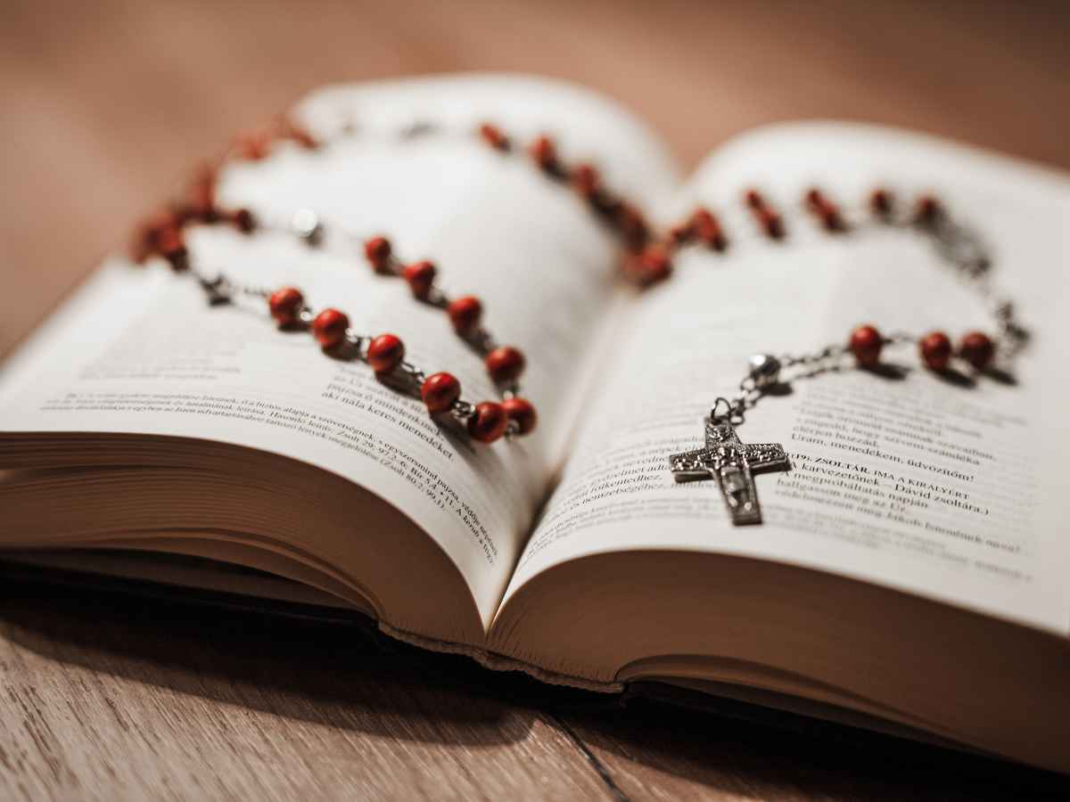 Bíblia aberta sobre mesa de madeira com um terço marrom e crucifixo repousando sobre as páginas