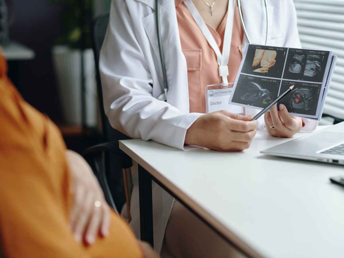 Médica sentada em consultório mostrando imagens de ultrassom para paciente grávida, apontando detalhes
