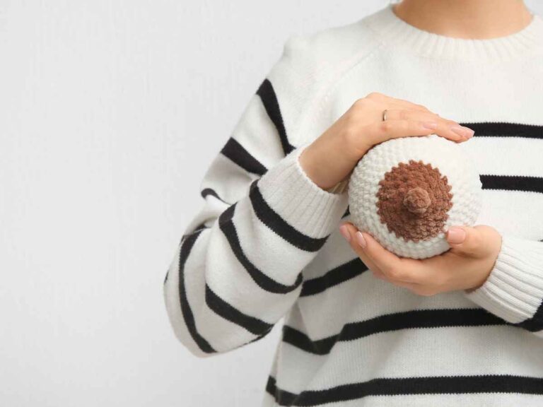 Mulher segurando seio de tricot com mamilo escurecido. Em frente a fundo sólido branco