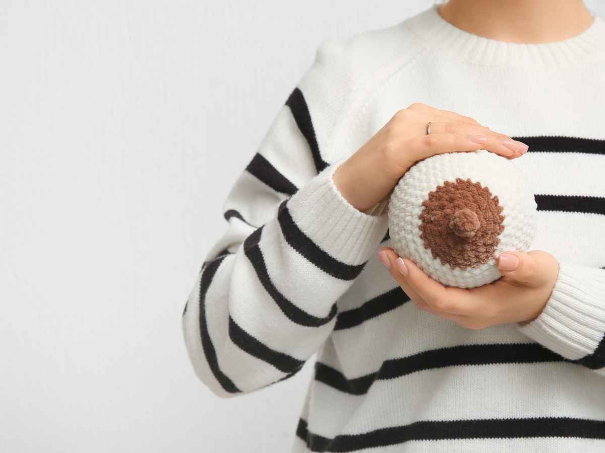 Mulher segurando seio de tricot com mamilo escurecido. Em frente a fundo sólido branco