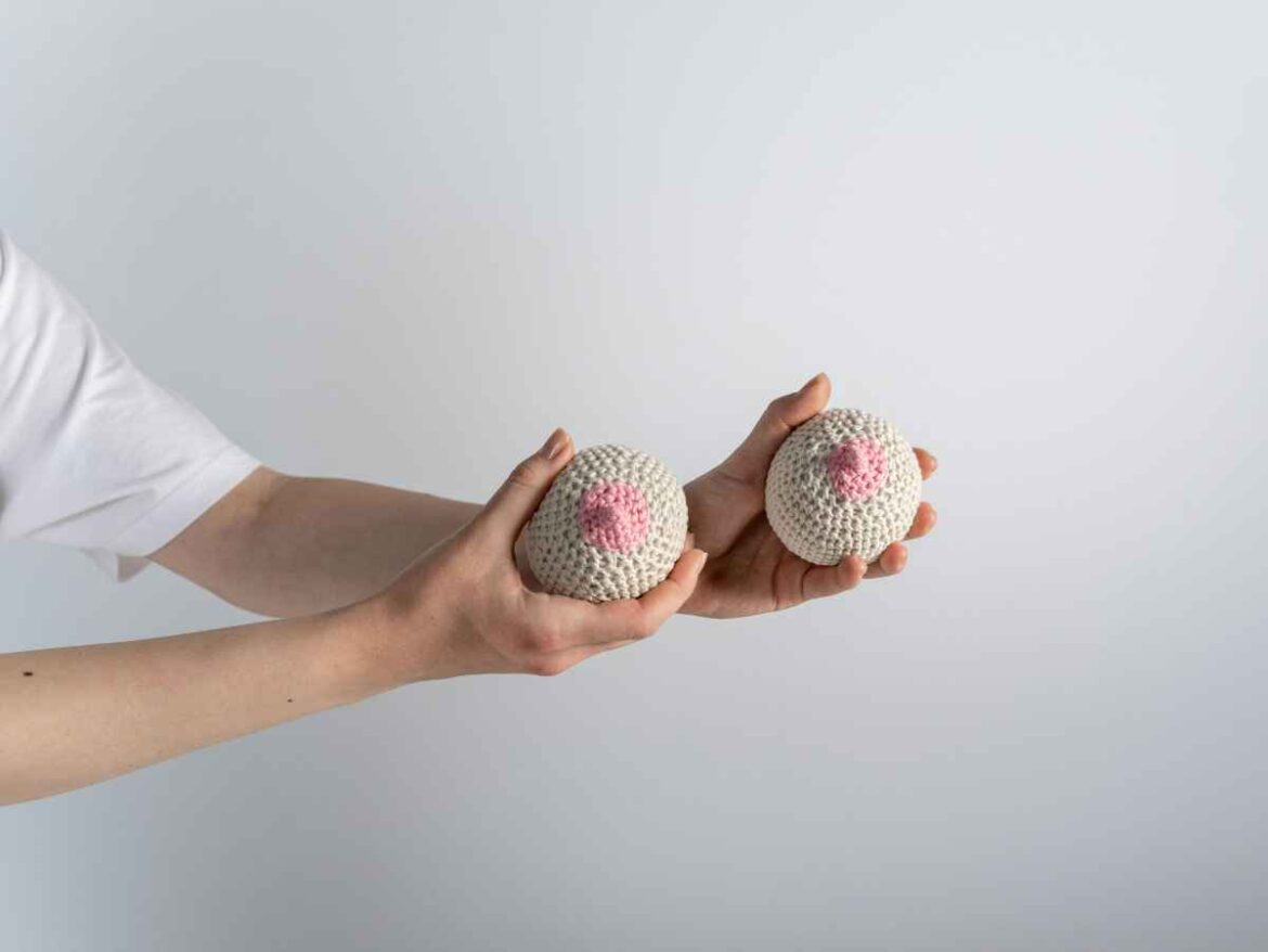 Pessoa segurando duas bolas de tricot que se assemelham a seios, simbolizando o escurecimento do mamilo