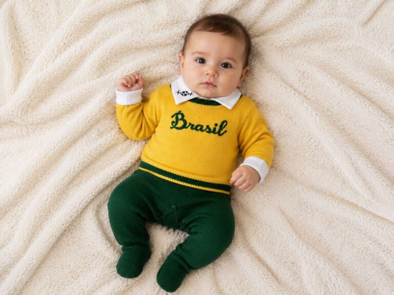 Bebê usando conjunto nas cores verde e amarelo com a palavra “Brasil” estampada na roupa, deitado sobre manta clara.