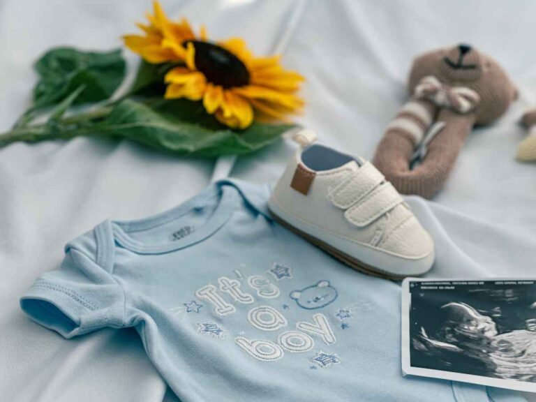 Roupa de bebê azul, sapatinho infantil e imagem de ultrassom sobre a cama