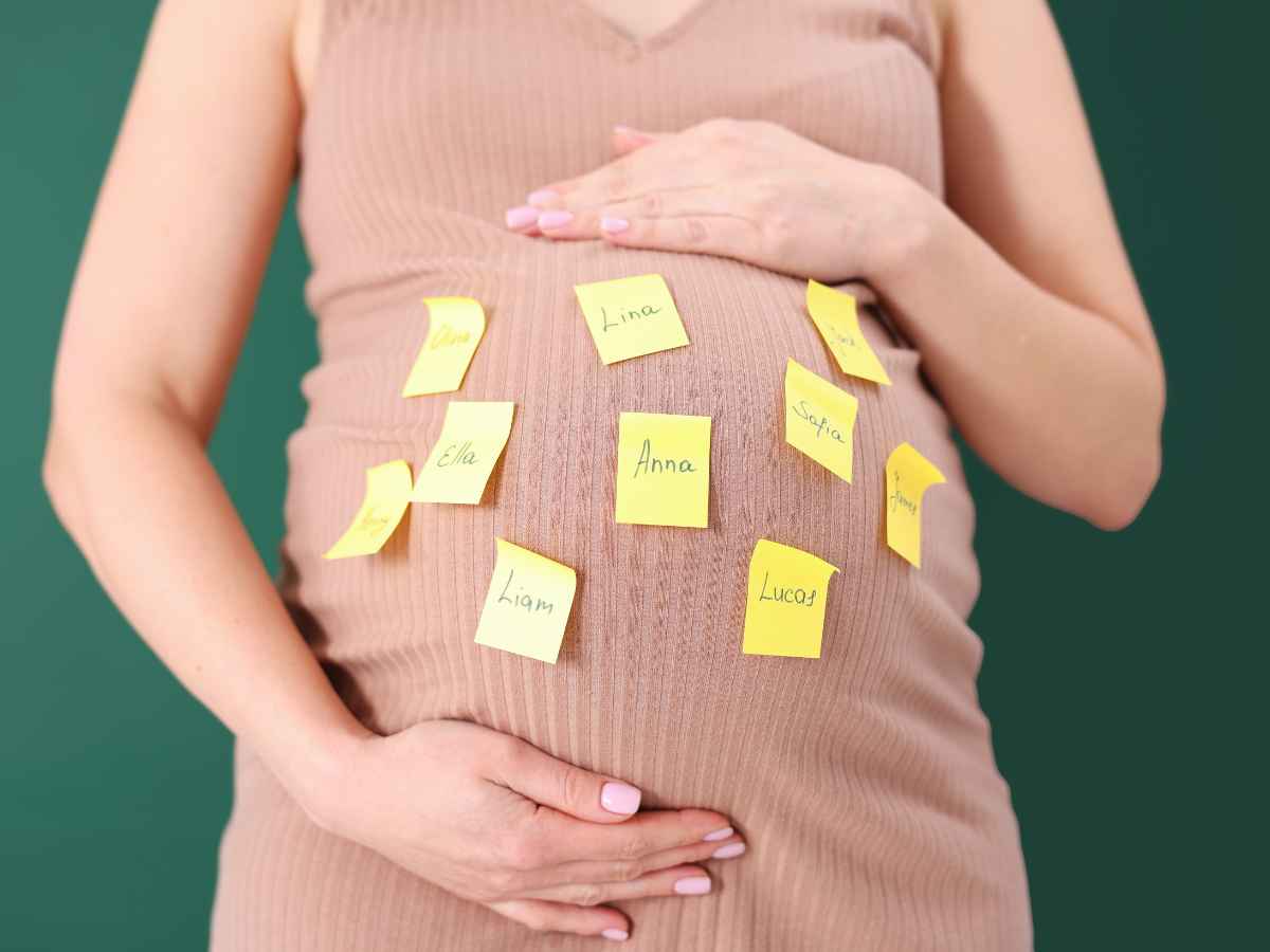 Gestante segurando a barriga com papéis adesivos contendo diferentes sugestões de nomes de bebê