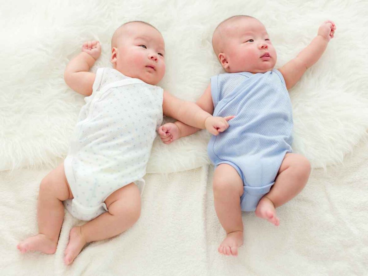 Bebês gêmeos deitados lado a lado usando bodies em tons claros de azul e branco