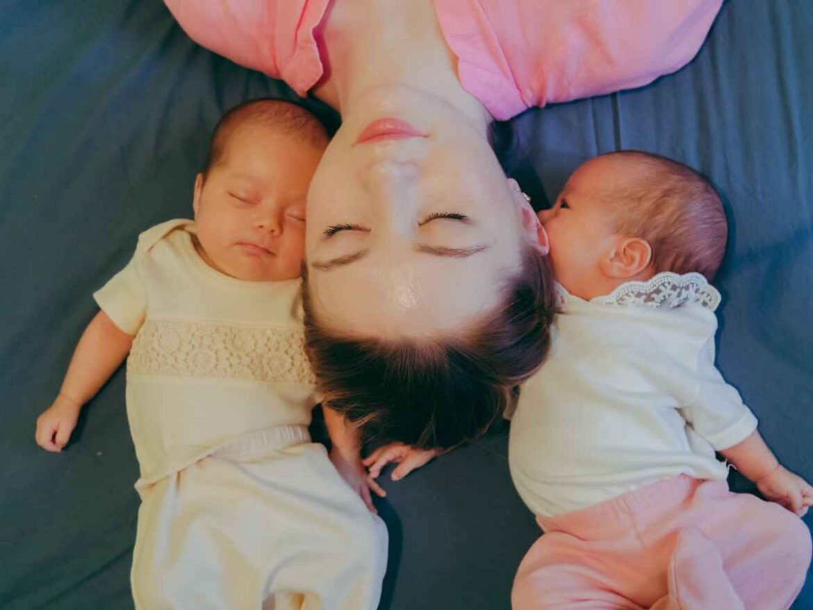 Mãe descansando ao lado de bebês gêmeos recém-nascidos deitados sobre cama