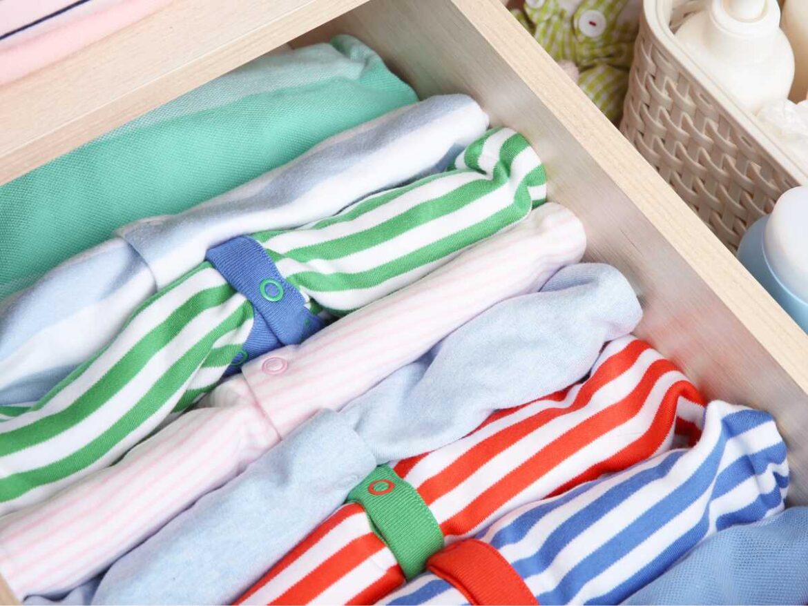 Roupa de bebê dobradas e organizadas dentro de uma gaveta. Ton verde, azul e vermelho